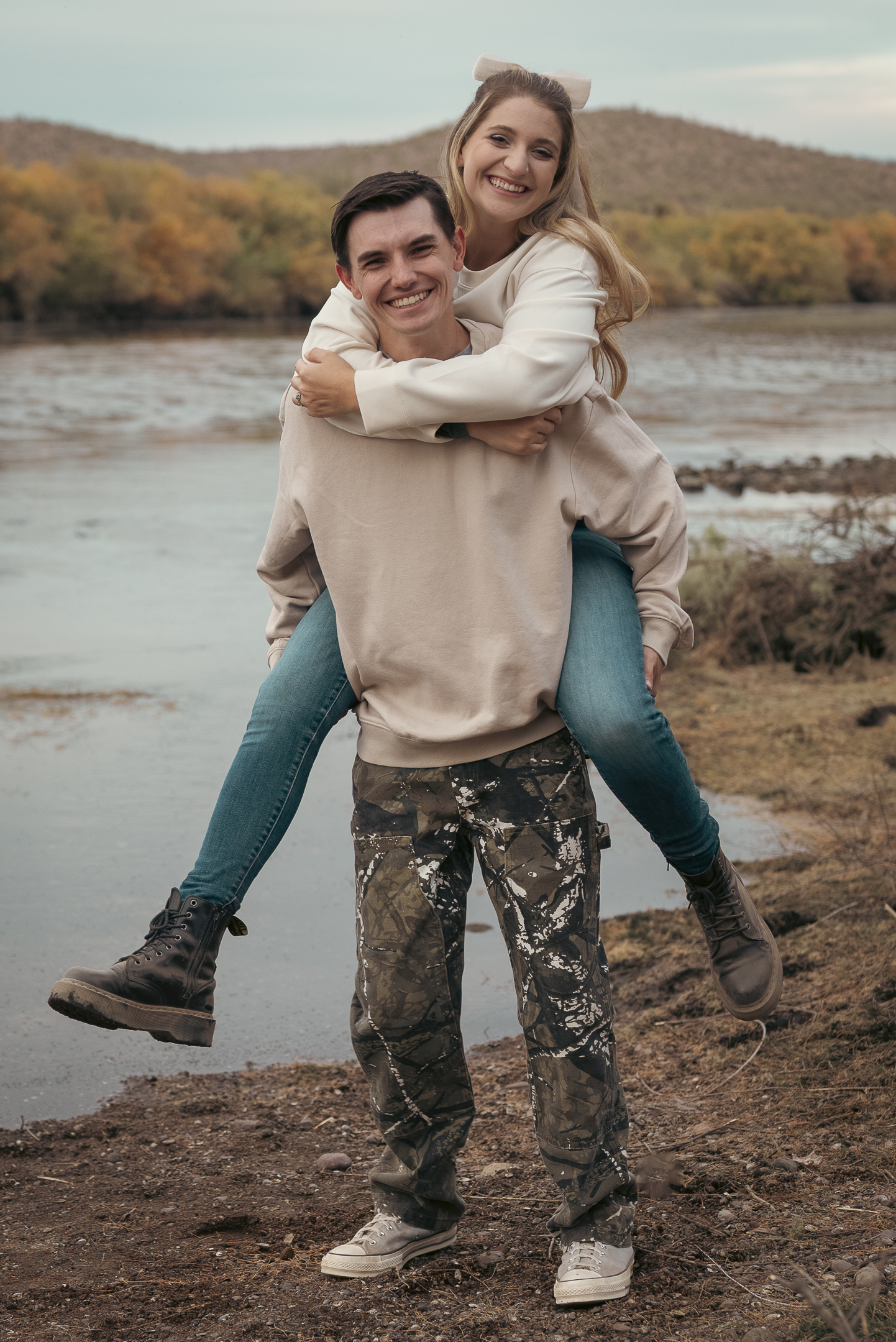 Engaged couple being playful as she rides on his back for photo by the Lower Salt River