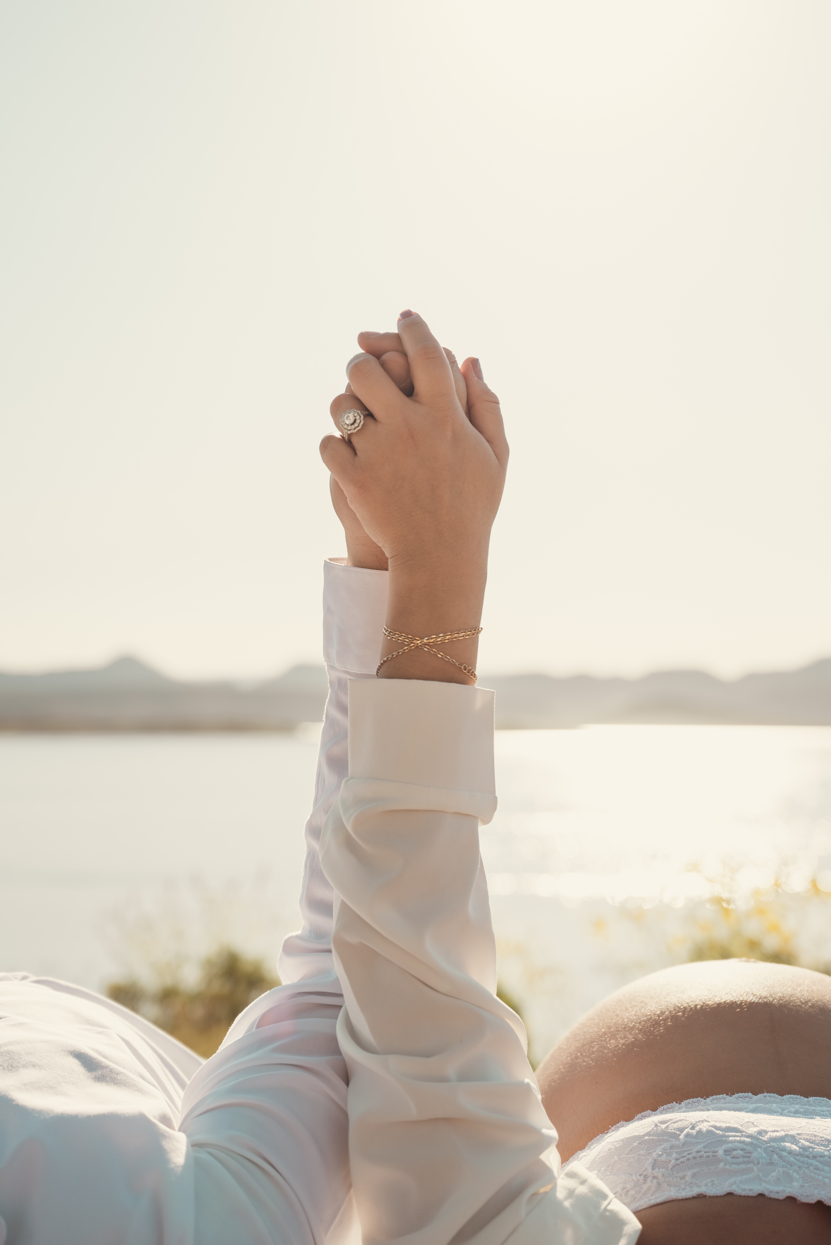Couple laying hands held pointed to the sky with exposed pregnant belly