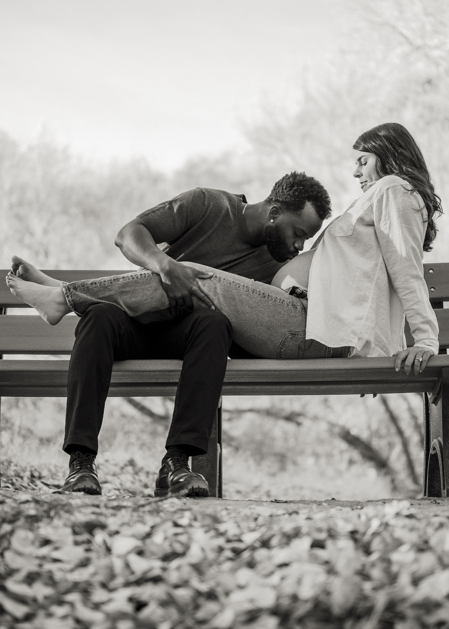 Couple sitting on bench, husband kissing wife's pregnant belly