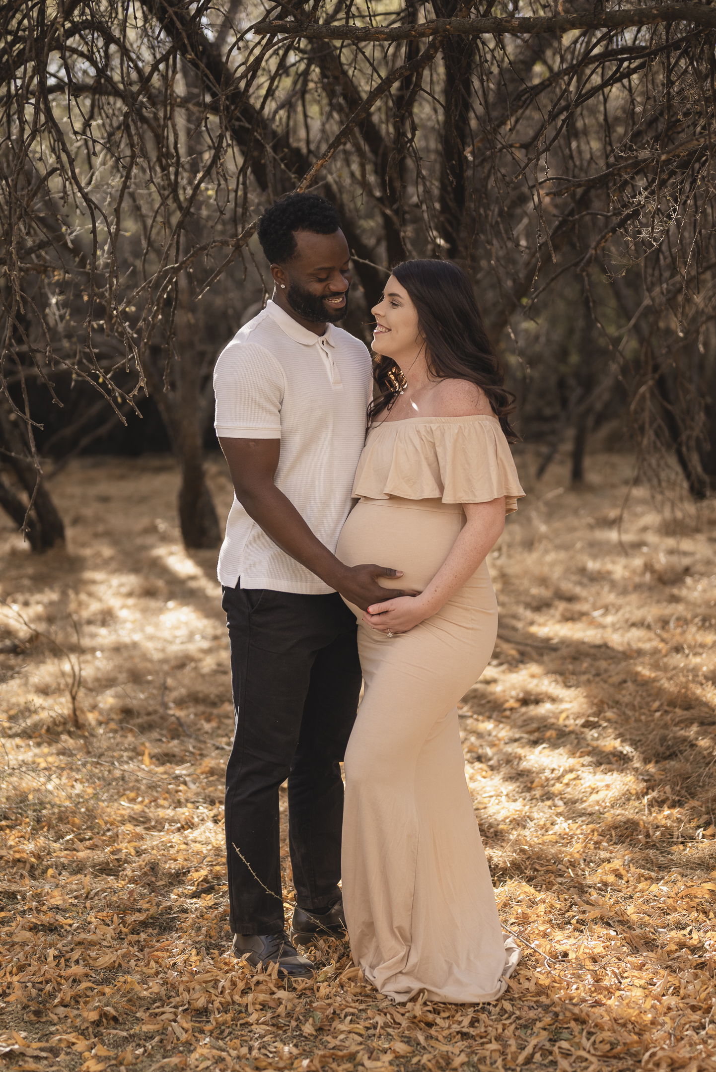 Couple holding pregnant belly in a natural setting with a mesquite forest in background
