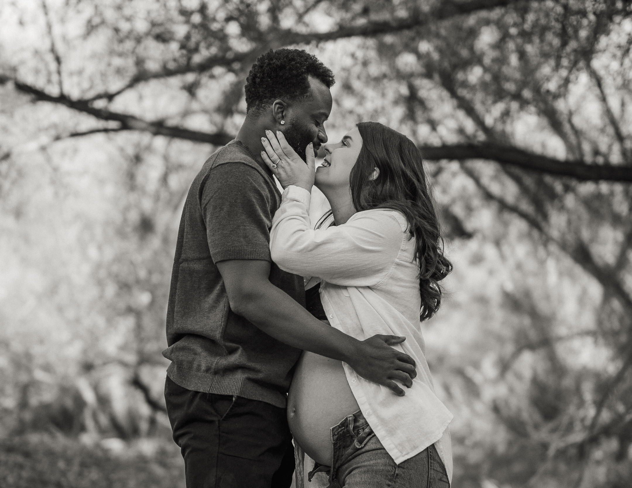 Black and white photo of couple embracing and leaning in to kiss with woman's pregnant belly exposed