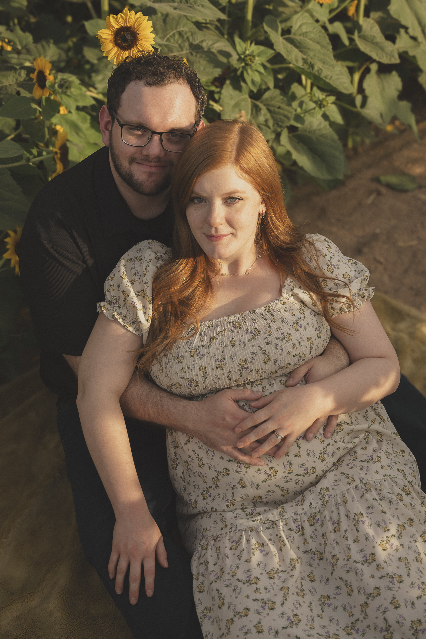 Couple sitting in sunflower field during maternity session