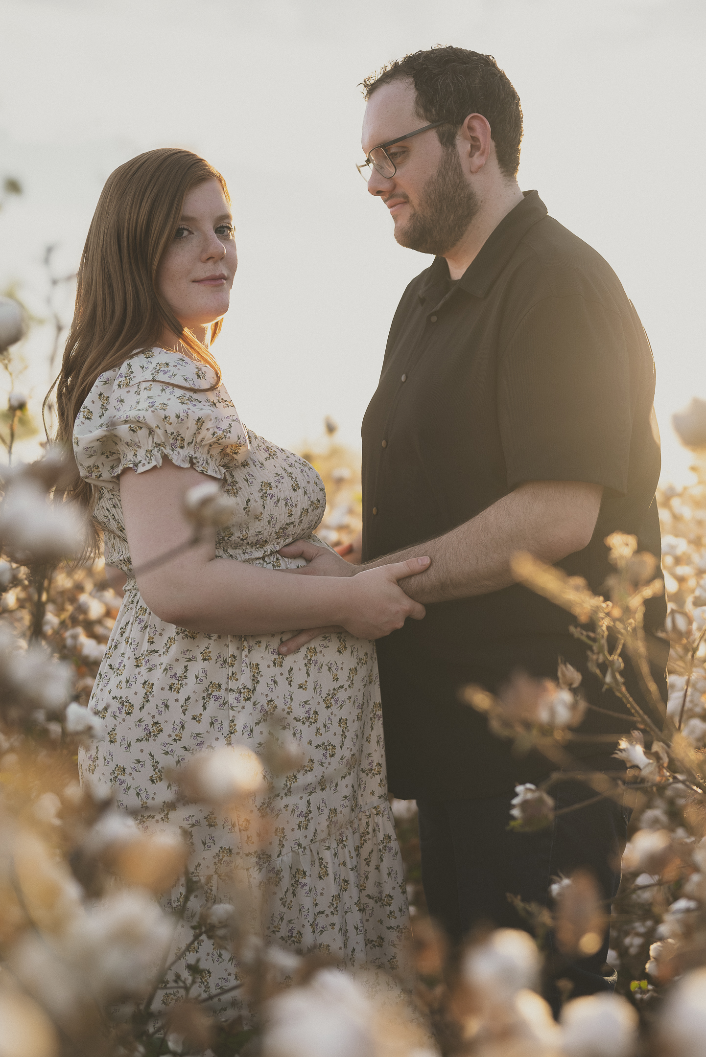 Pregnant couple standing in cottonfield at golden hour for maternity session in Buckeye, Arizona