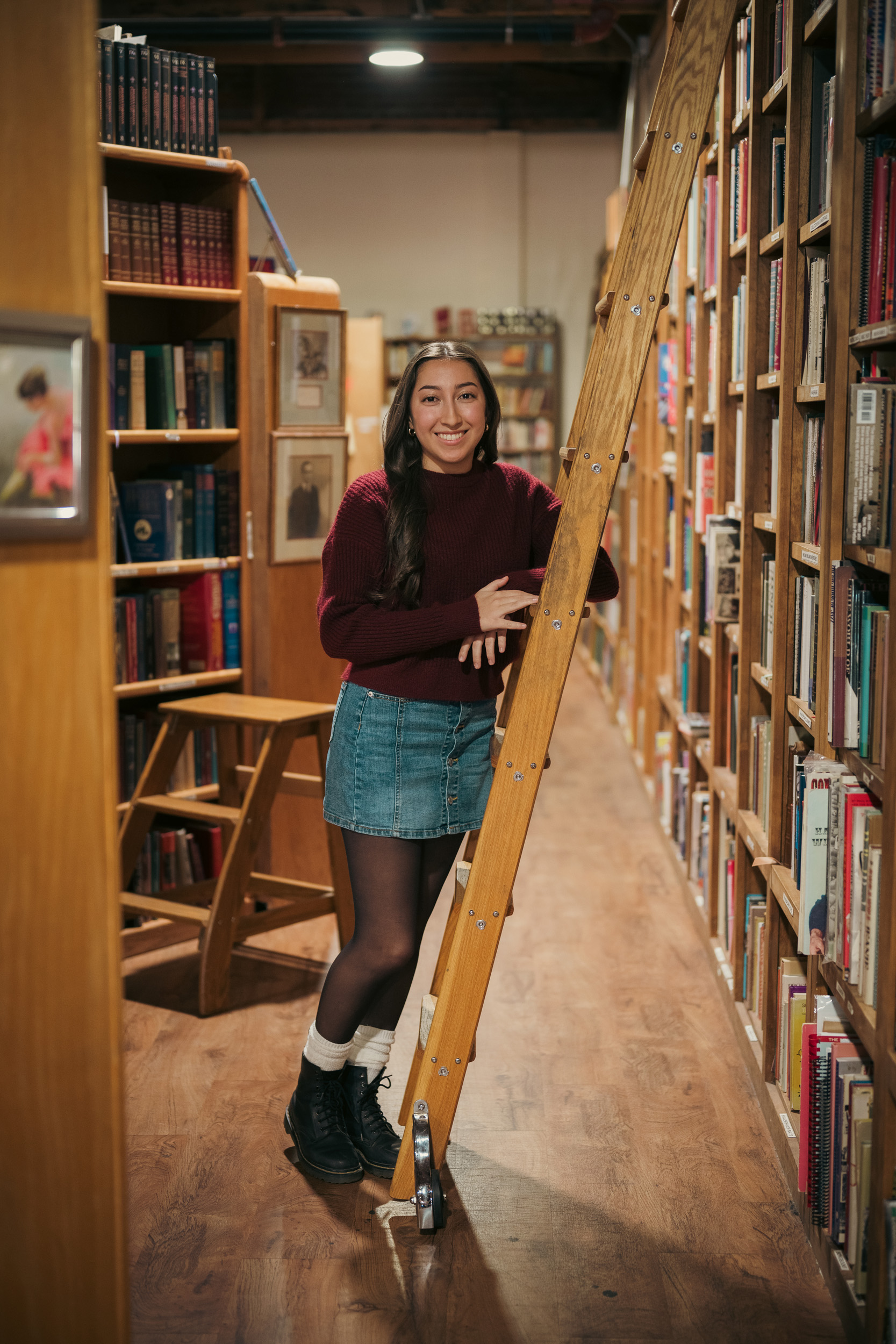 Senior Portrait leaning against ladder between bookshelves at Phoenix Arizona Book Gallery.