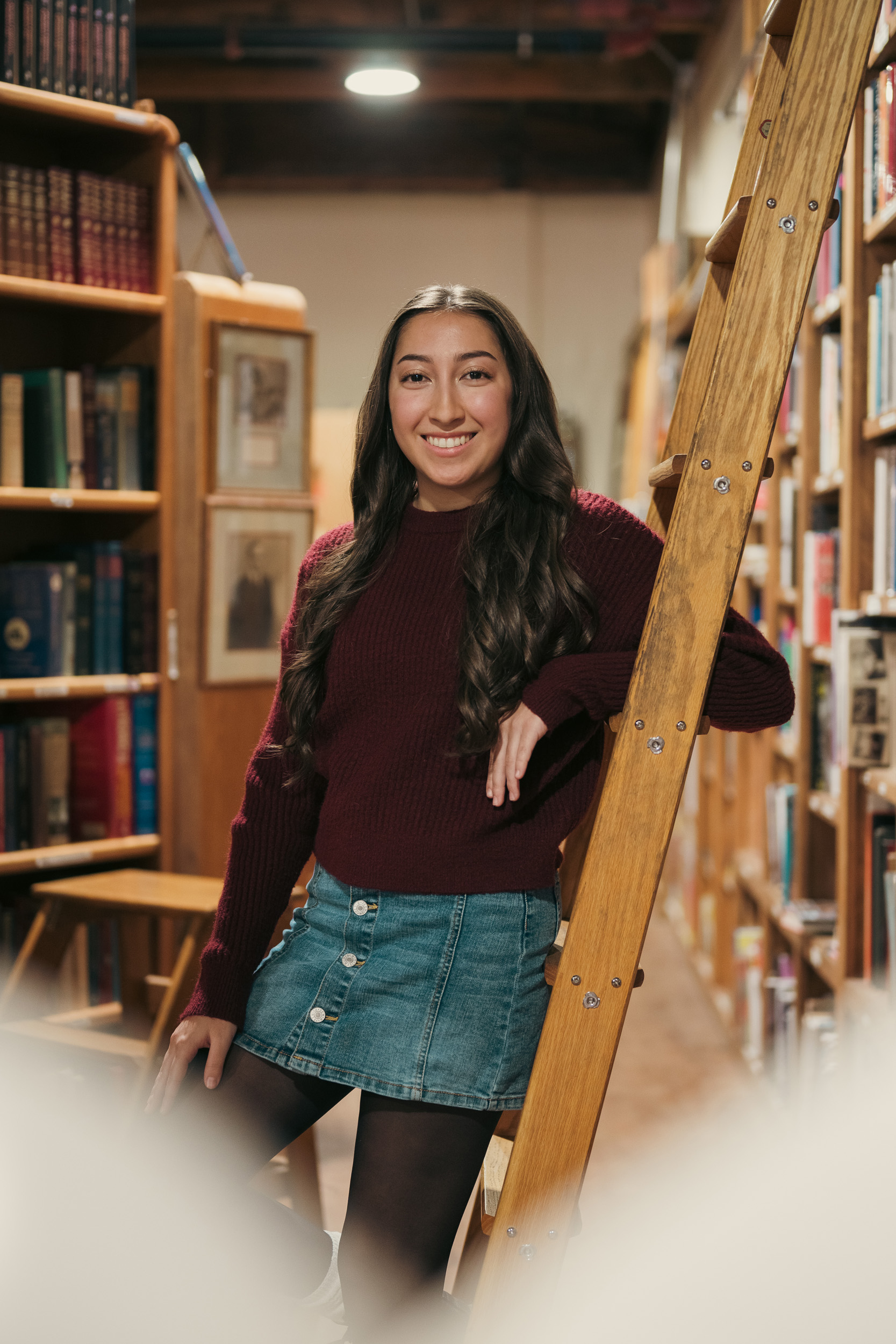 Senior Portrait leaning against ladder between bookshelves at Phoenix Arizona Book Gallery.