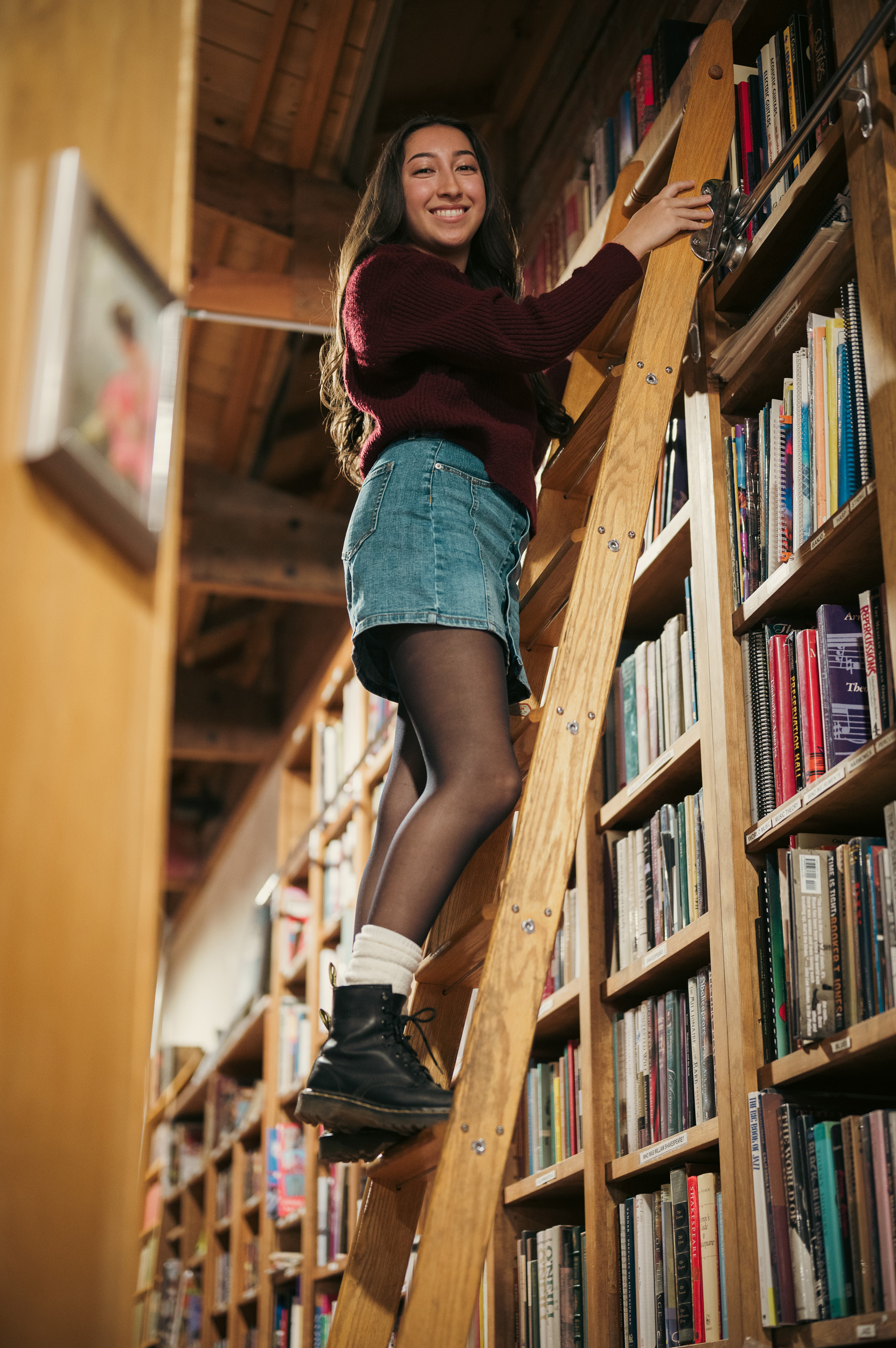 Senior Portrait leaning against ladder between bookshelves at Phoenix Arizona Book Gallery.