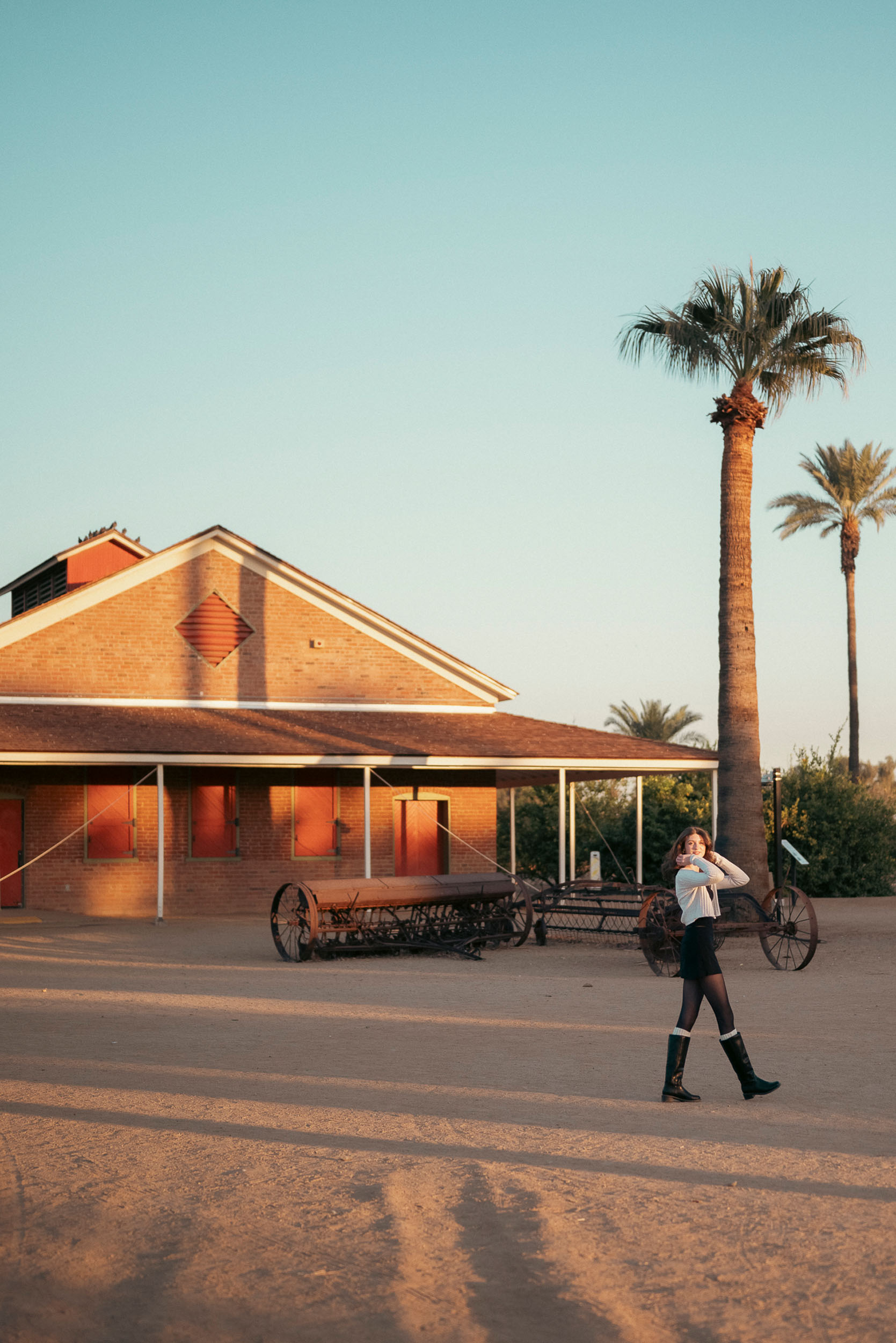 Senior photo of young woman walking through Sahuaro Ranch Park Glendale, AZ at golden hour.