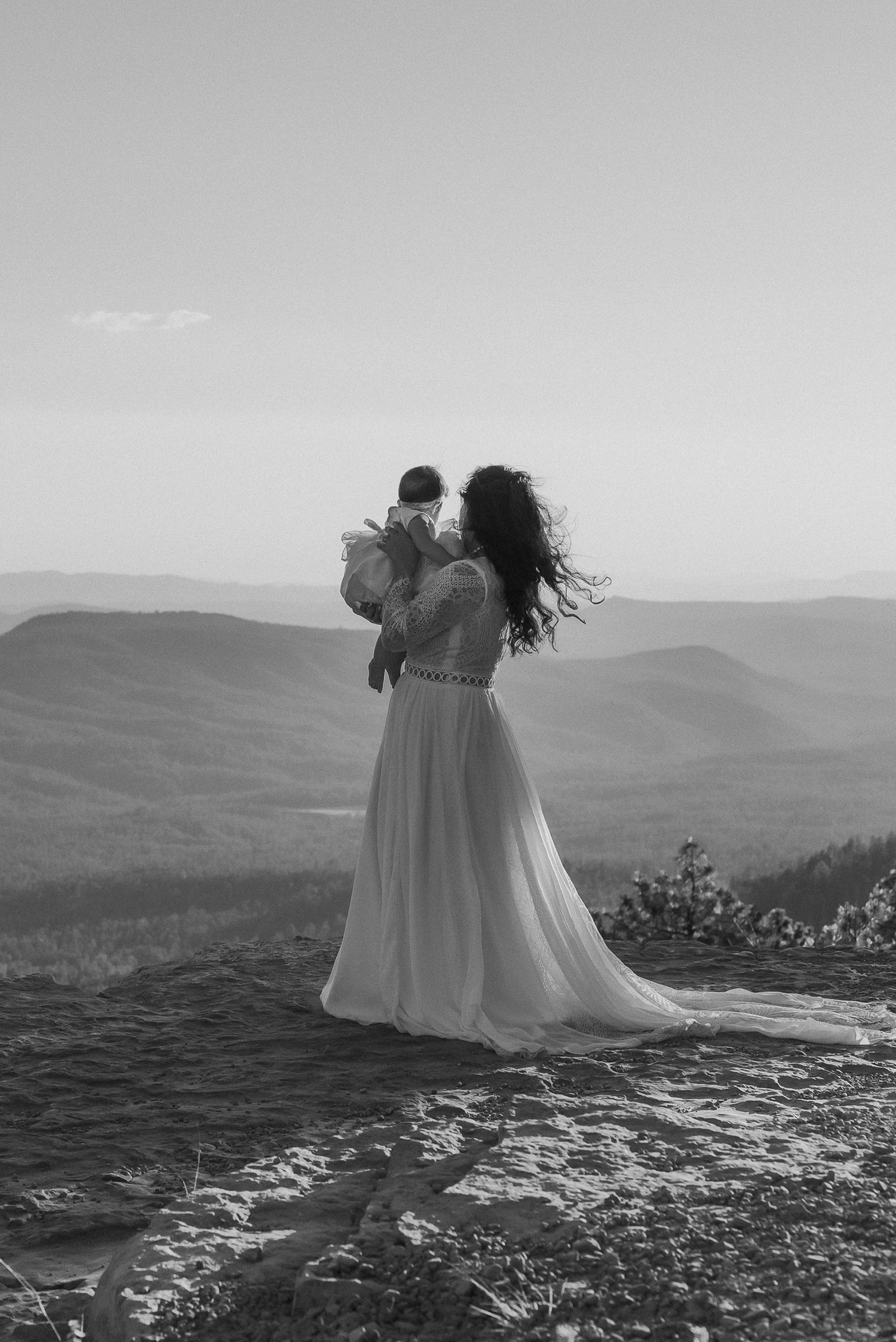 Bride holding baby looking out to the beautiful forest mountain overlook during elopement wedding at the Mogollon Rim in Payson, Arizona