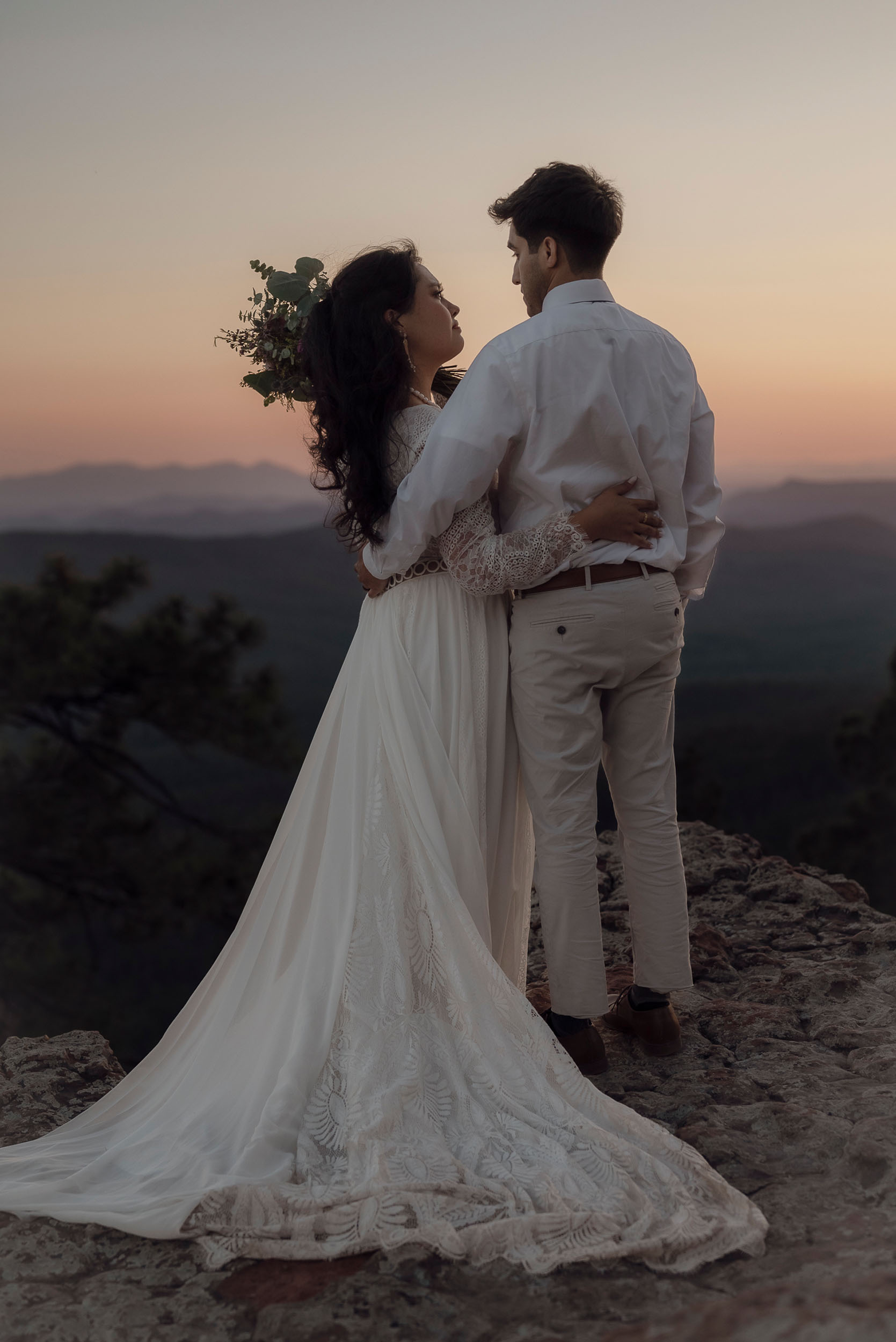 Bride and groom embrace looking out onto expansive mountain forest views during elopement wedding at the Mogollon Rim in Payson, Arizona