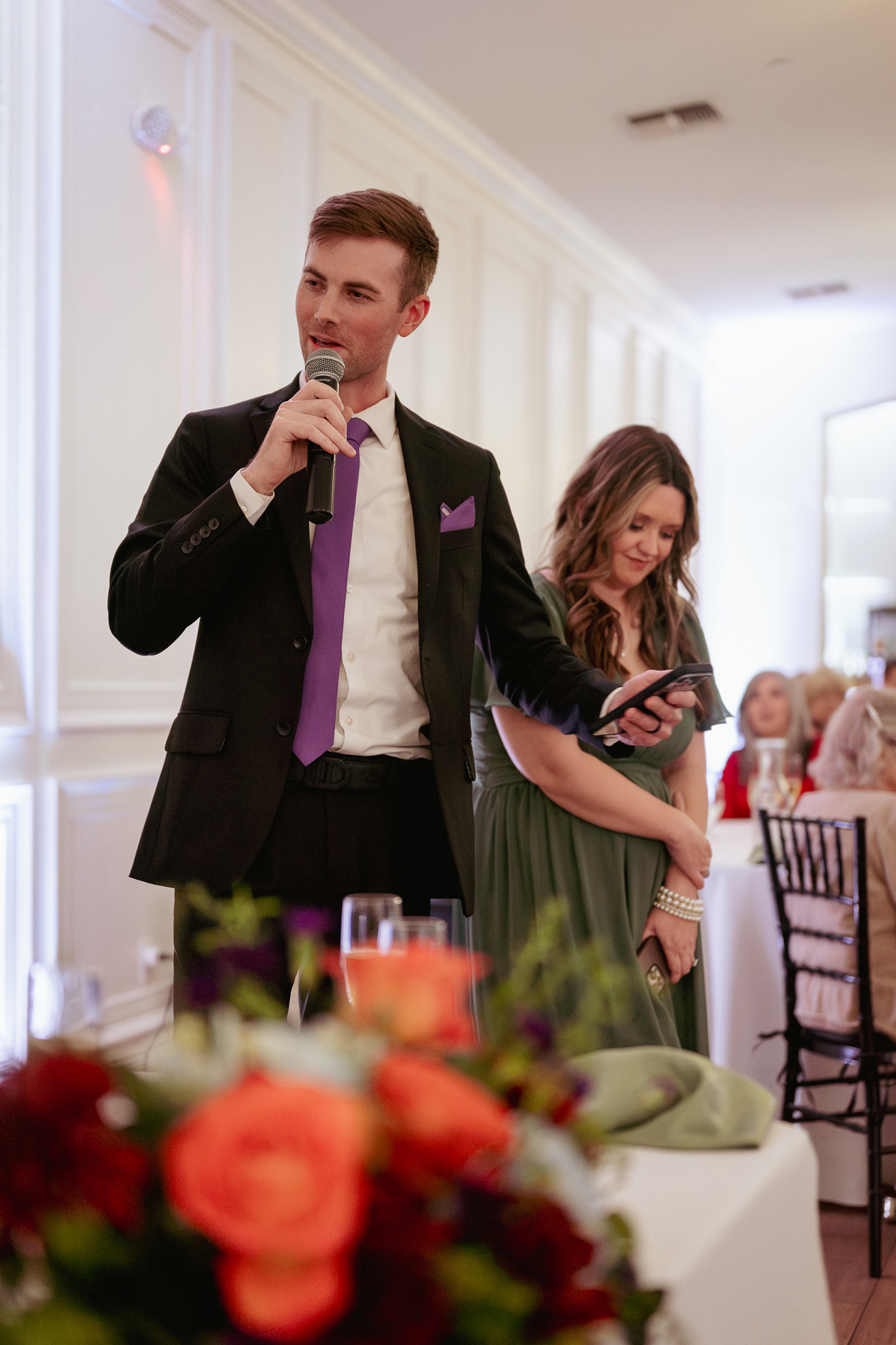 Groomsman and bridesmaid give speeches at wedding reception.