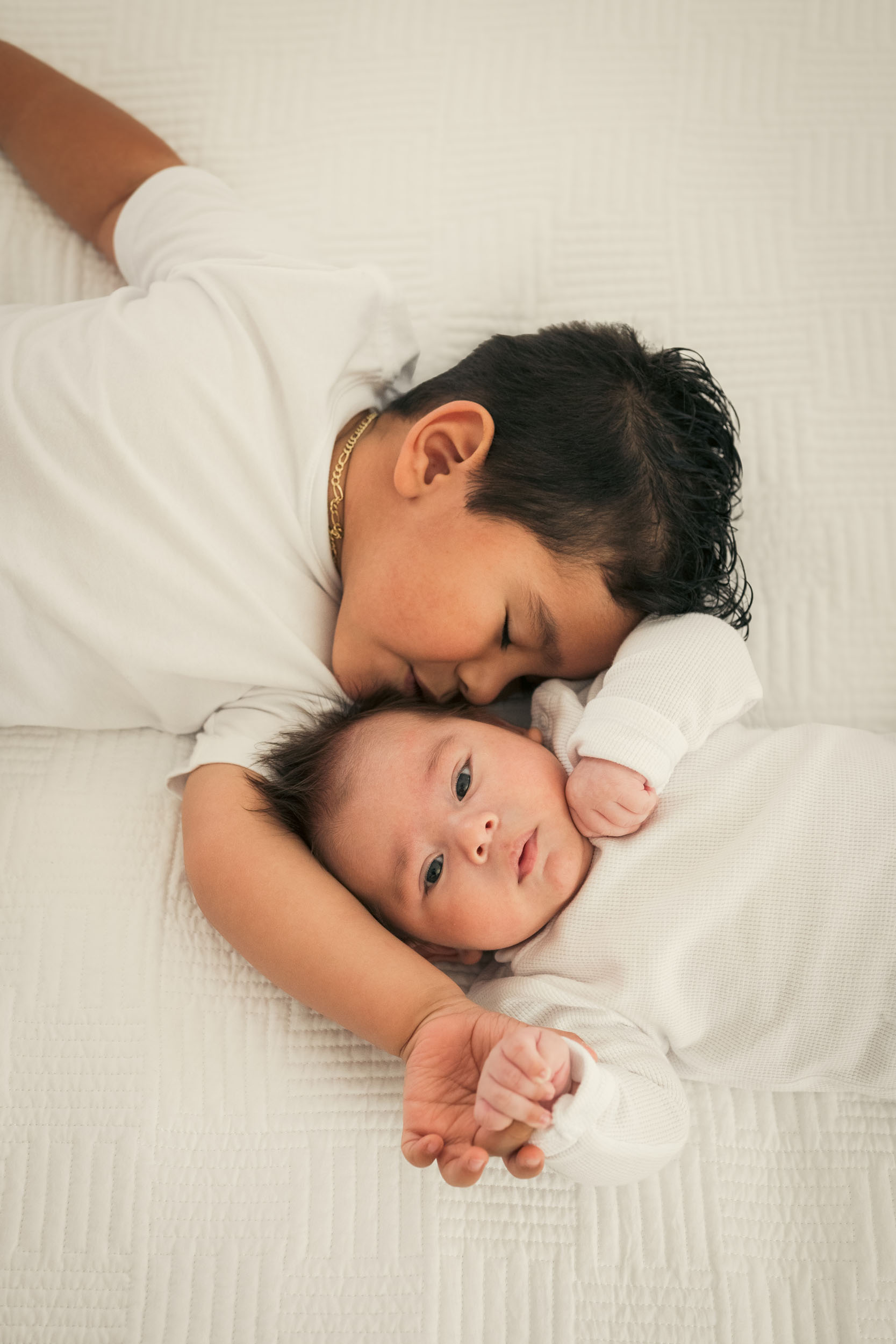 young boy giving baby brother a kiss laying down during lifestyle photo session