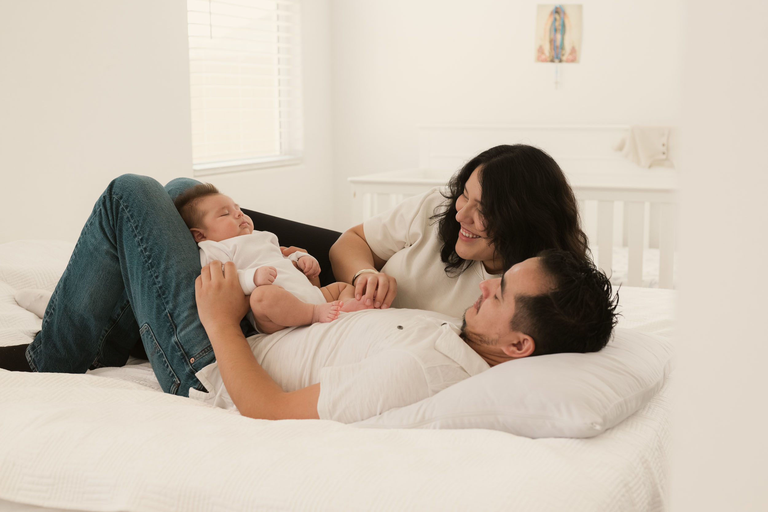 mother and father laying on bed with baby while smiling and admiring lovingly during lifestyle photo session