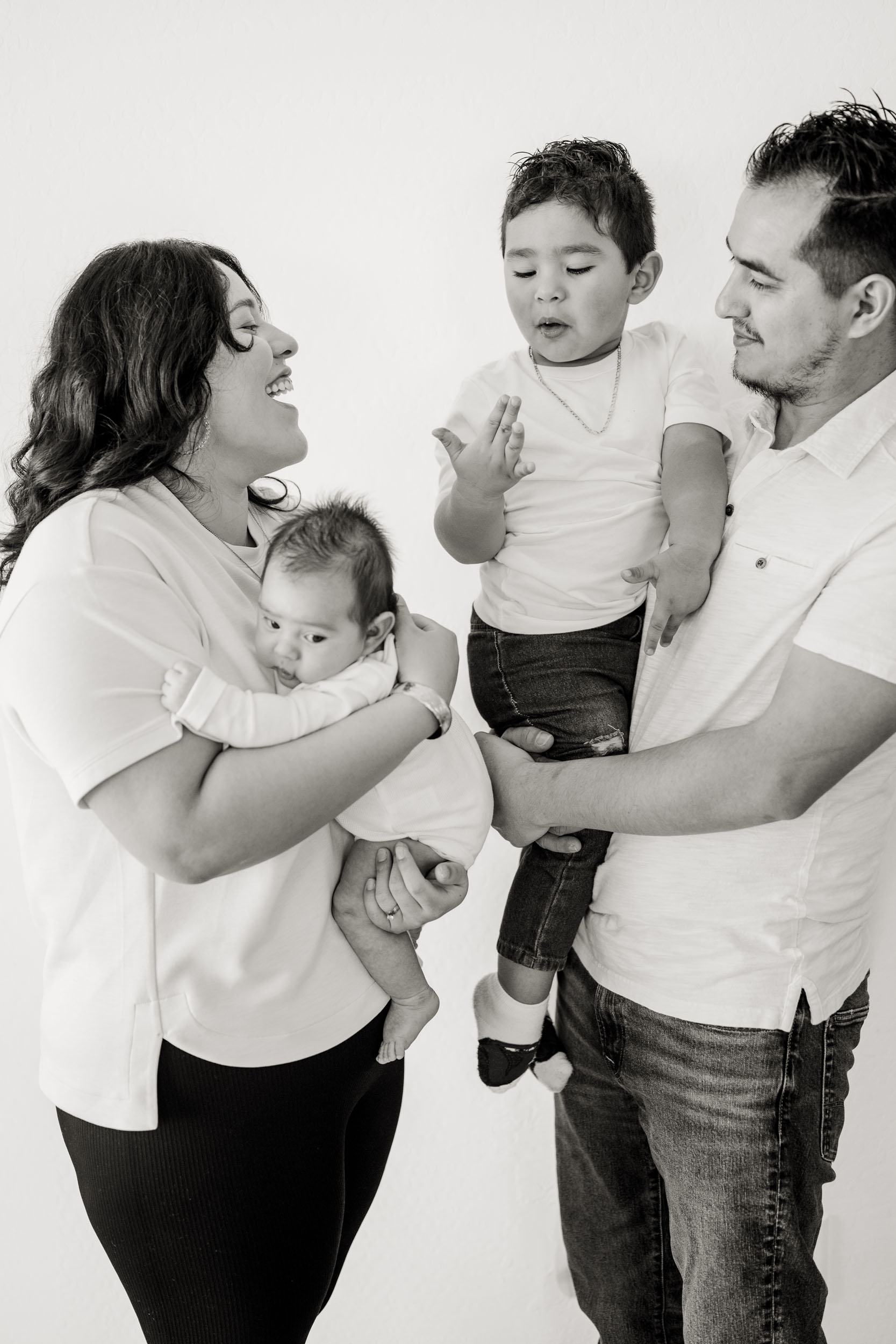 black and white family portrait of parents holding newborn baby and young son.