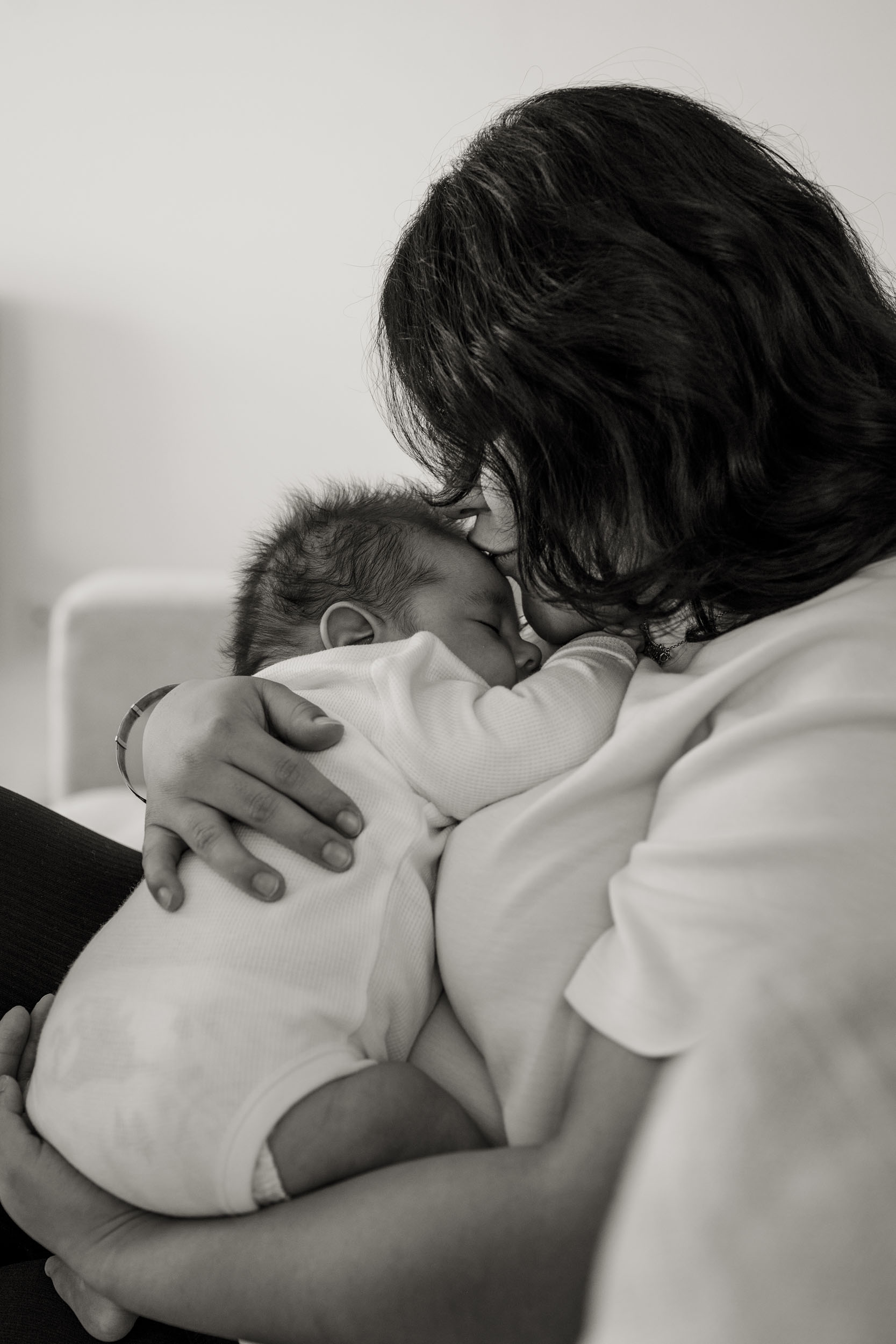 baby sleeping on mother's chest and mother kissing his forehead