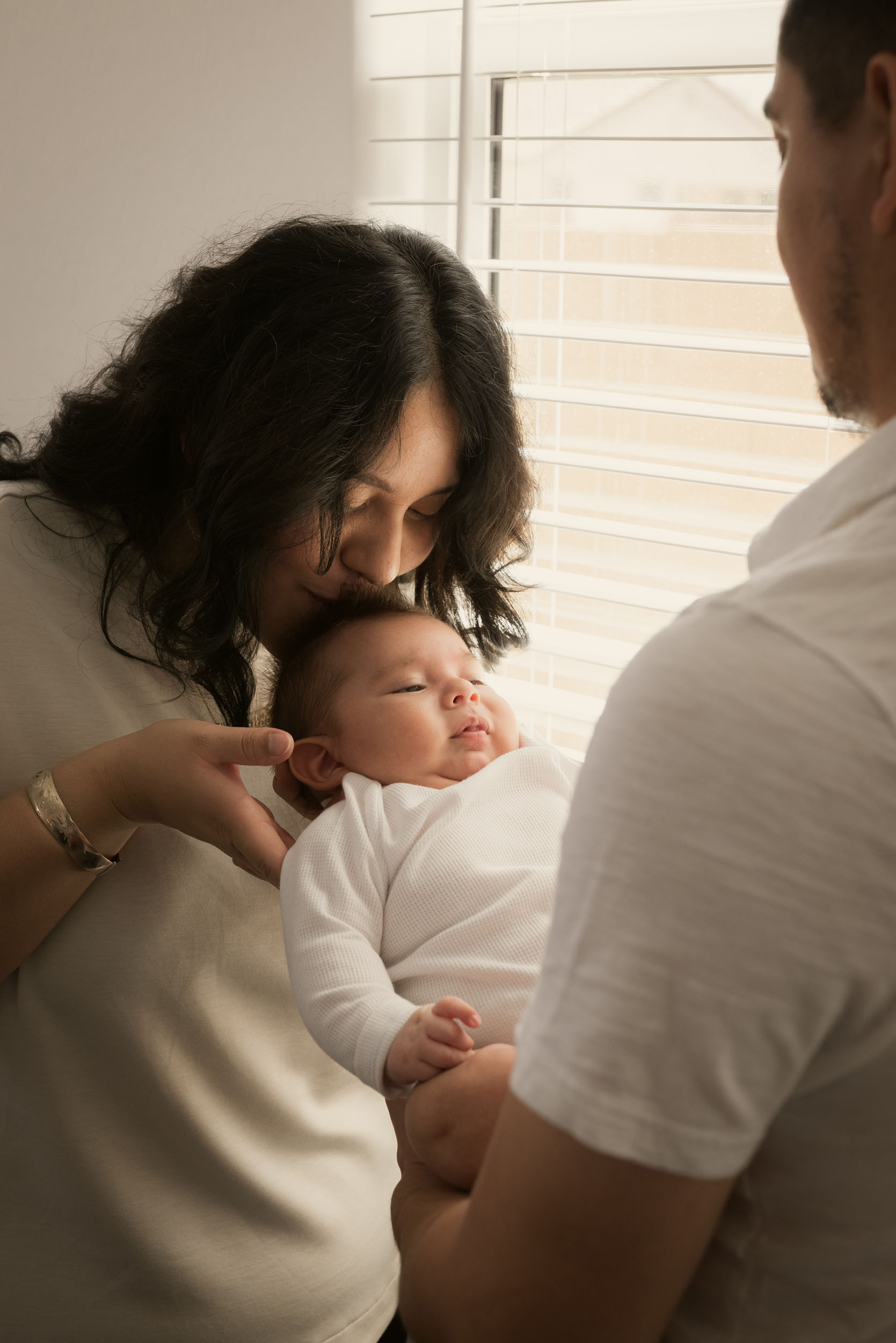 mother kissing baby on head as father holds him at home during photoshoot in arizona