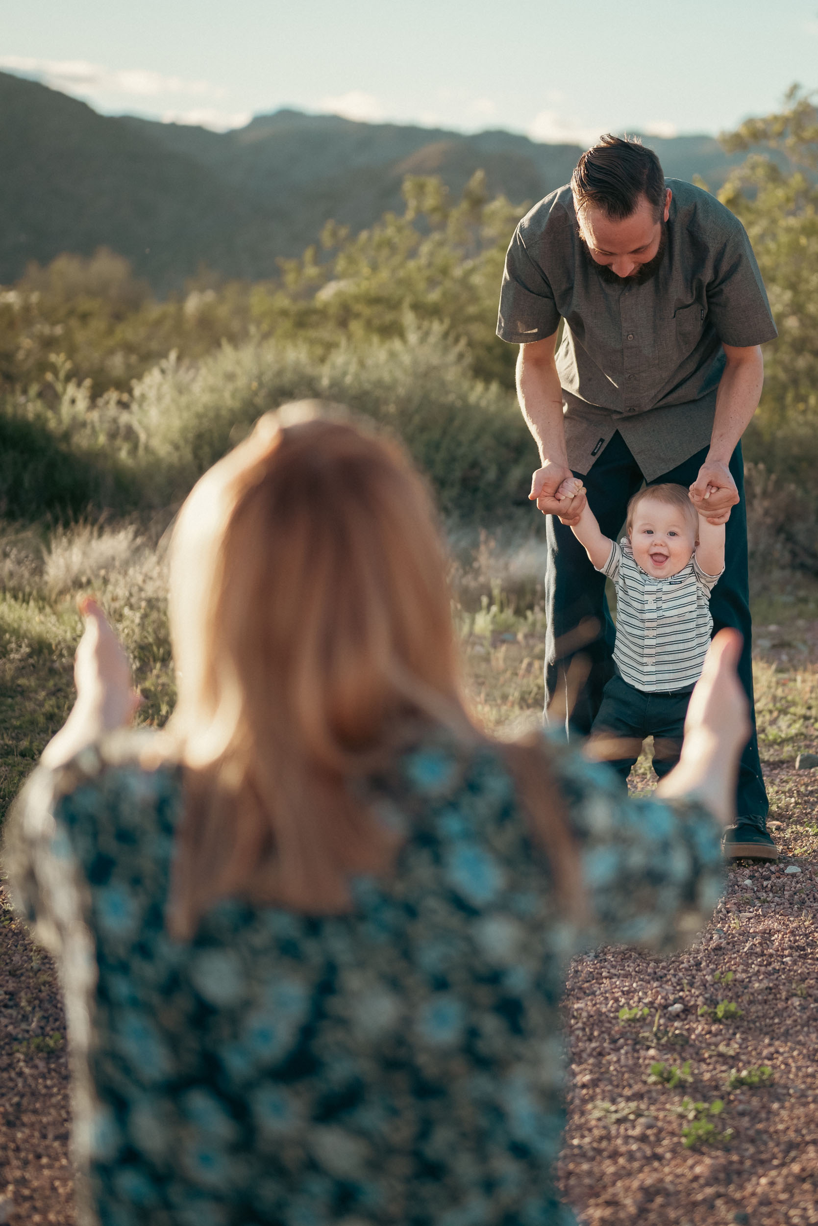 mother in the foreground extending arms towards her baby son and husband walking towards her at the White Tank Mountain Regional Park.