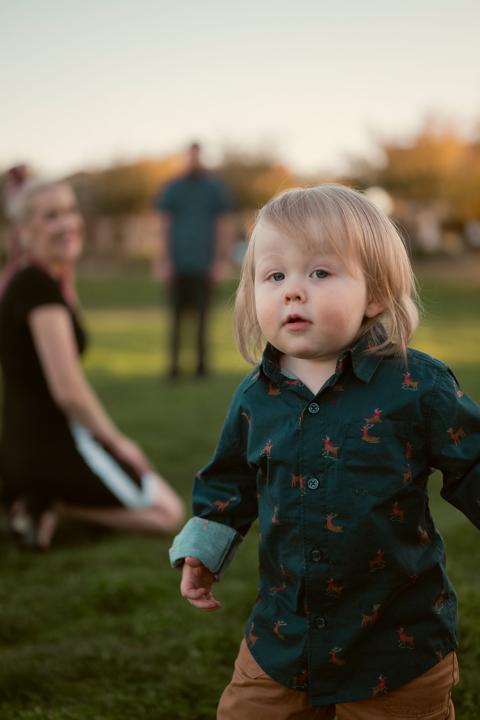 Toddler looking at the camera with parents in backdrop observing