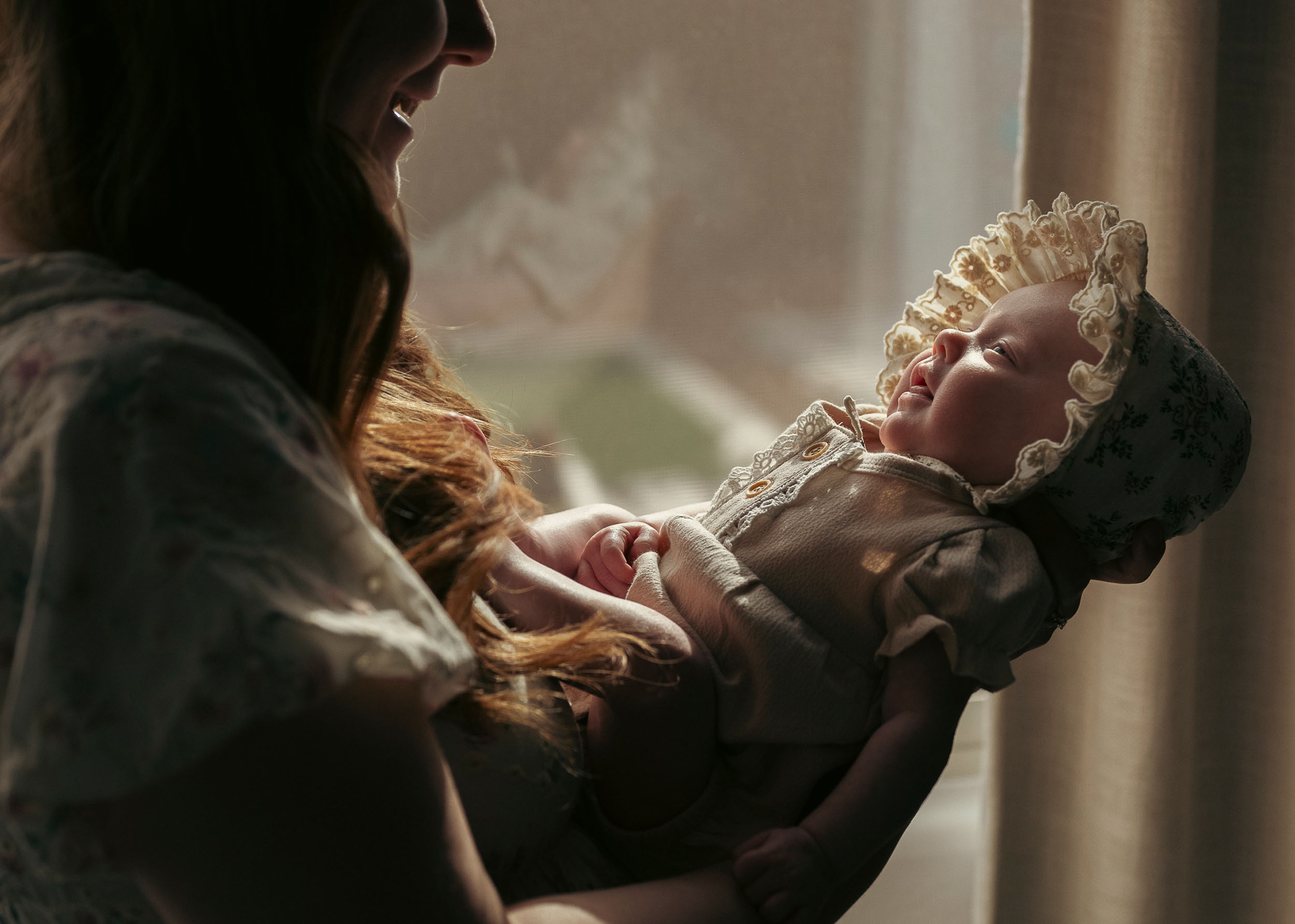 mother holding baby by window during newborn session