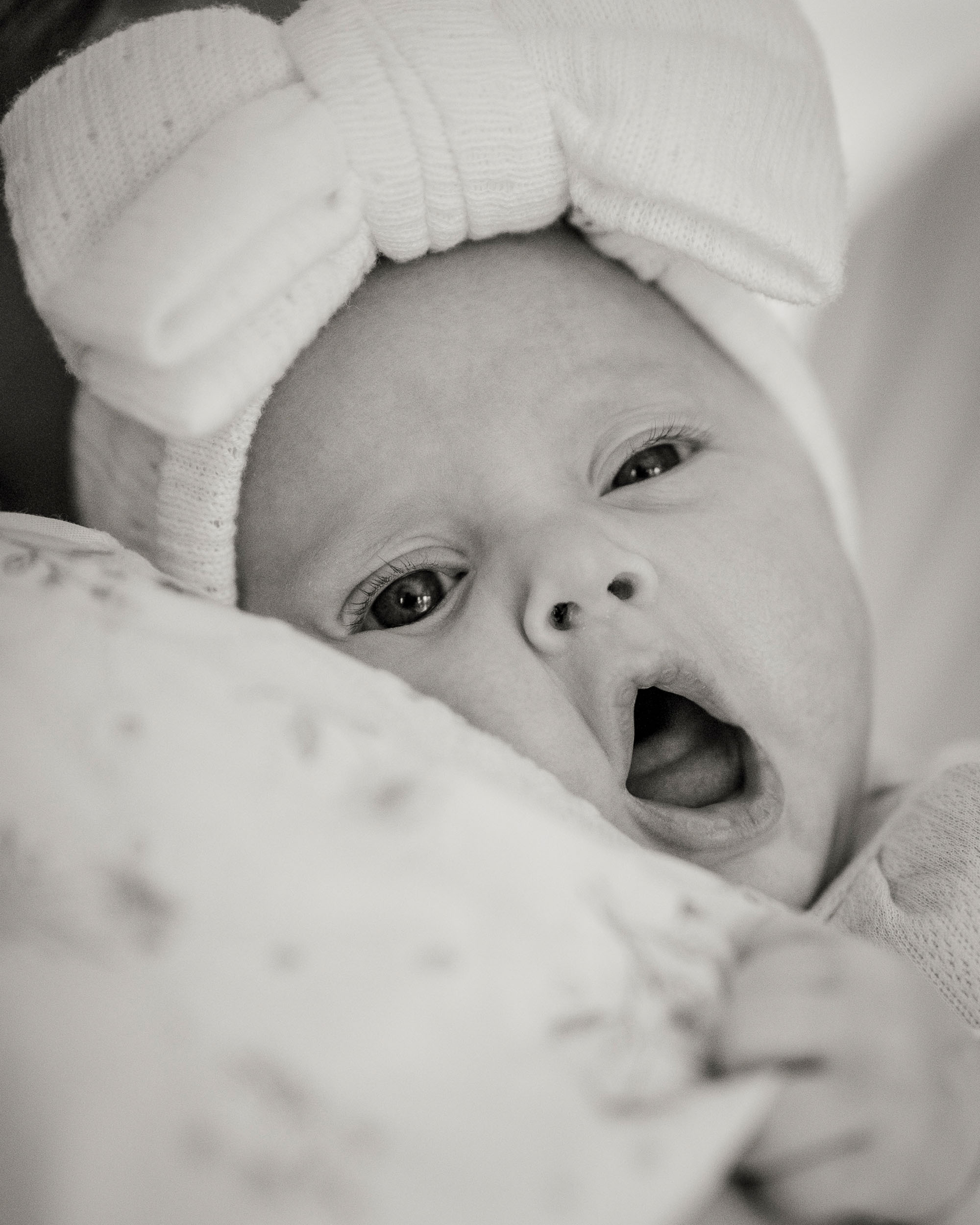 black and white photo of baby wearing bow yawning