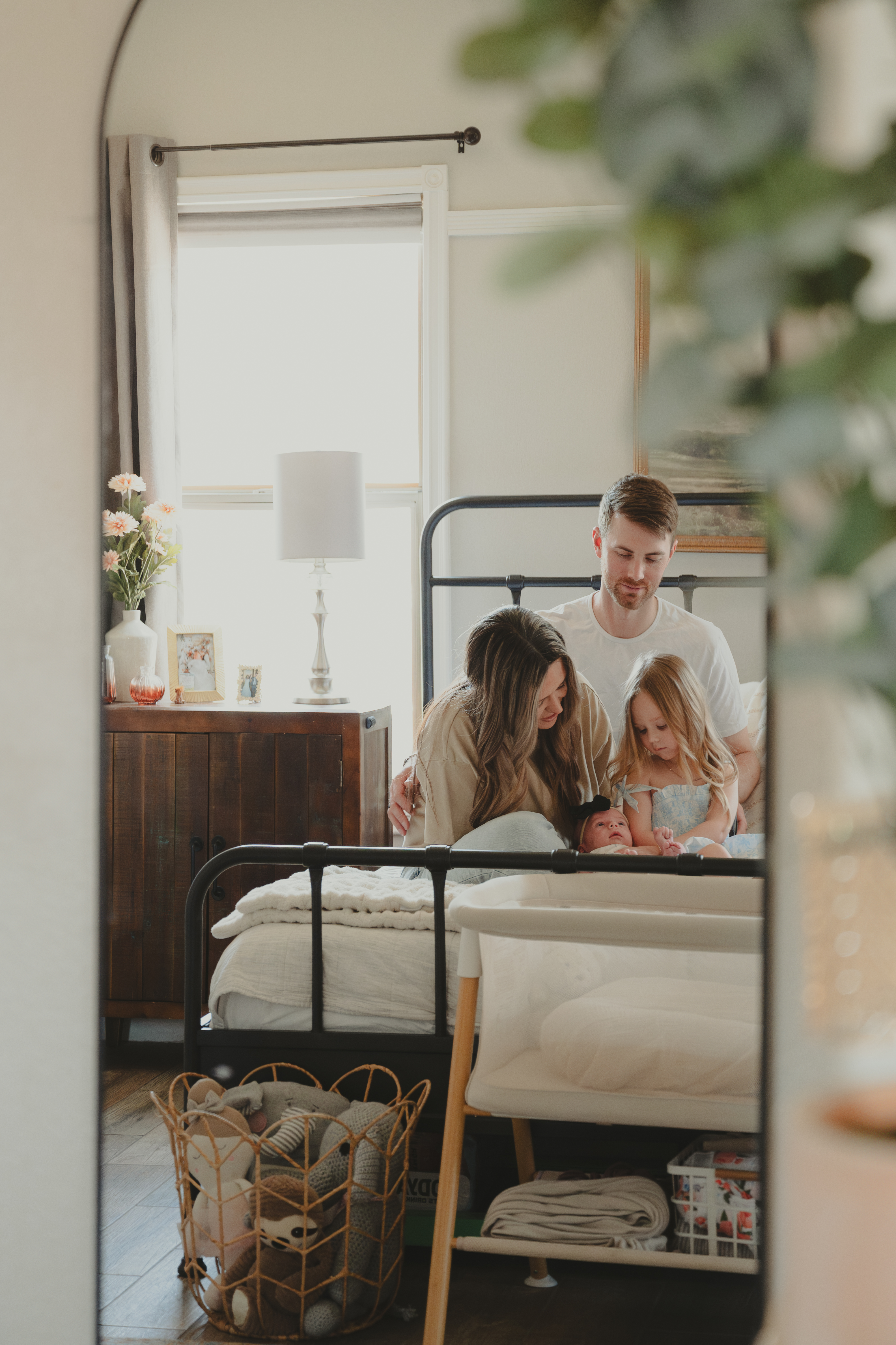 Mirror reflection of family sitting together on their bed with their newborn baby for Lifestyle family portraits.