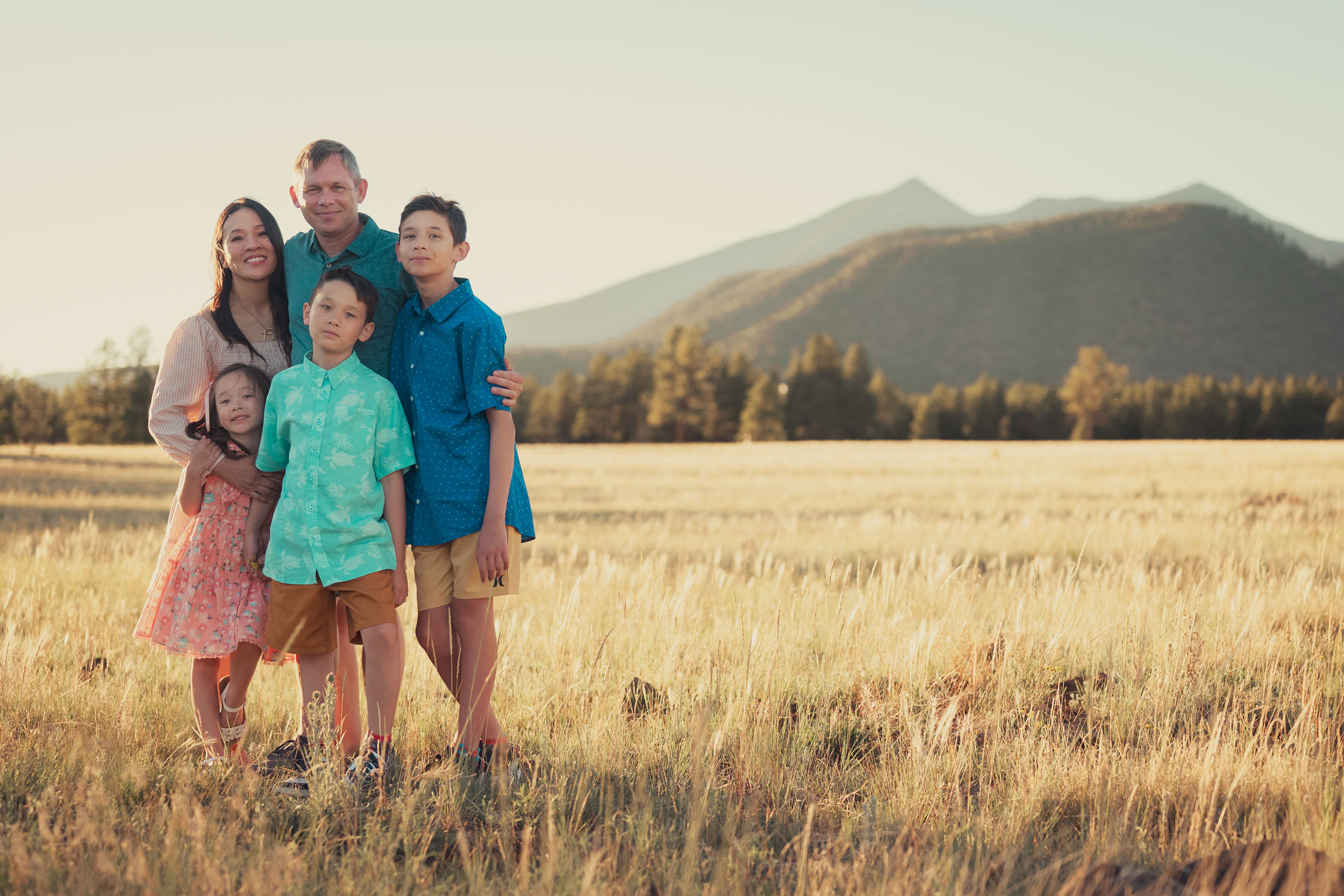 Family portrait at golden hour in a grassy meadow with pine trees and mountain landscape in the background