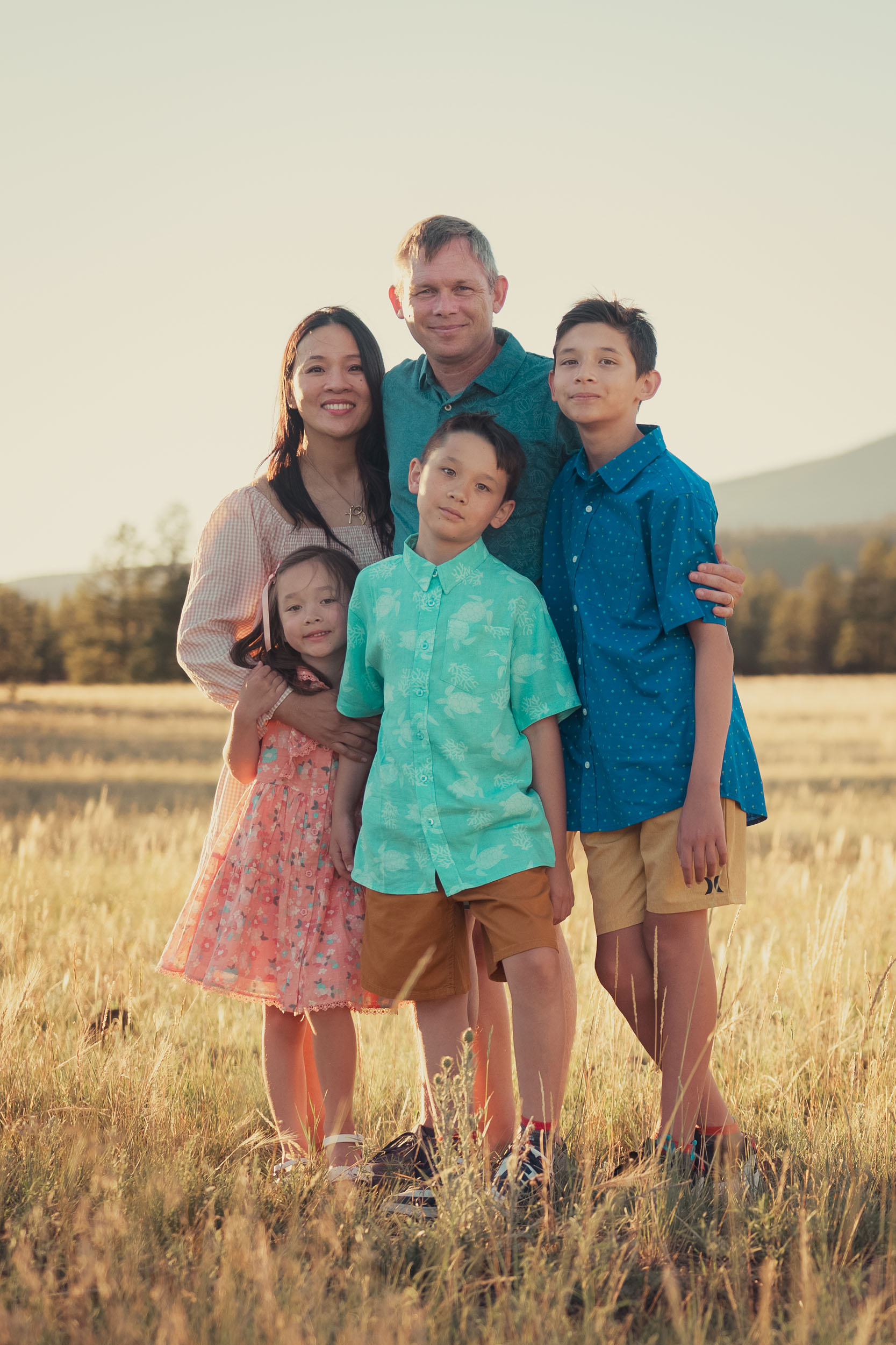 Family portrait at golden hour in a grassy meadow with pine trees and mountains in the background