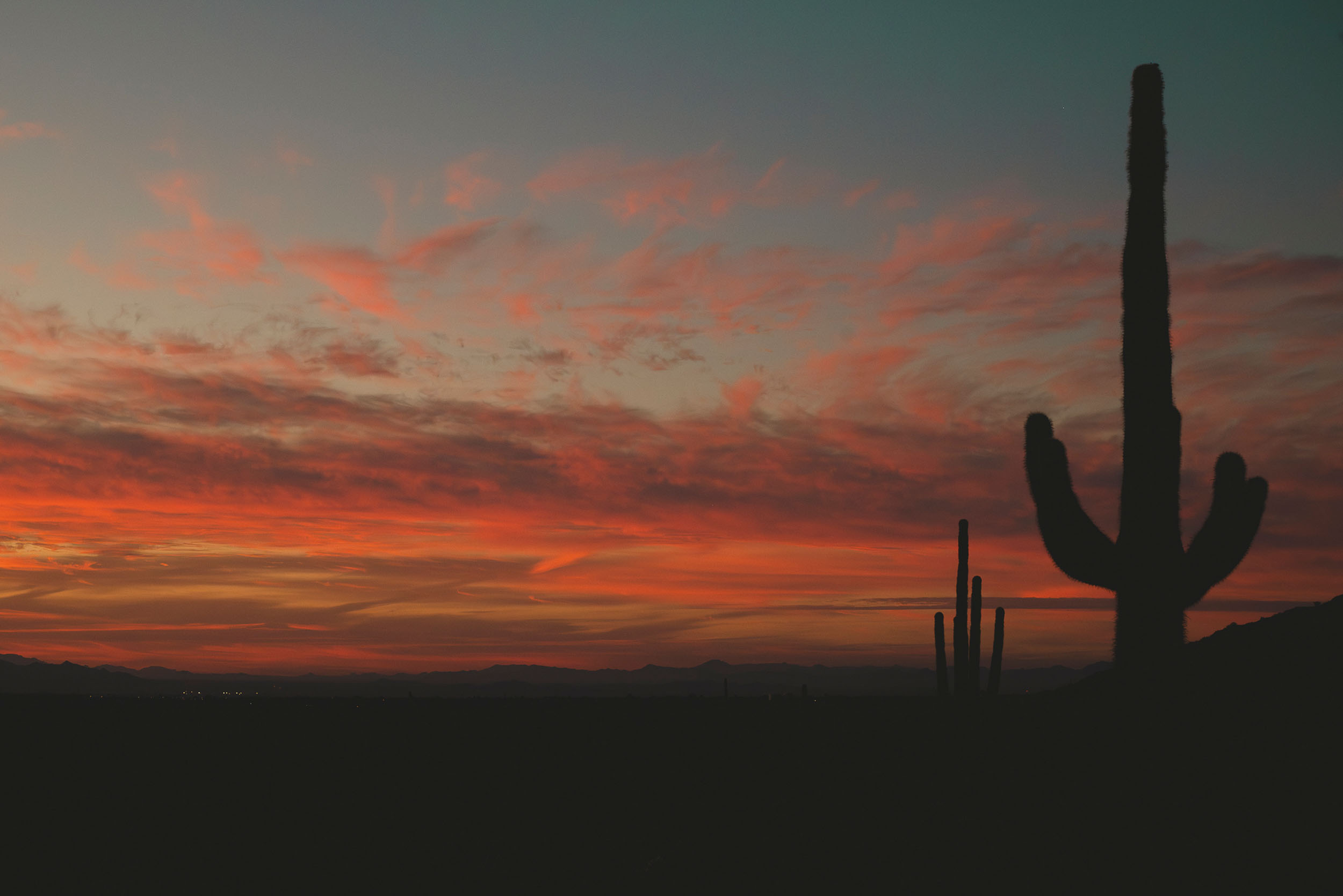 Colorful, desert sunrise with saguaro cactus silhouettes and mountains in the far distance.