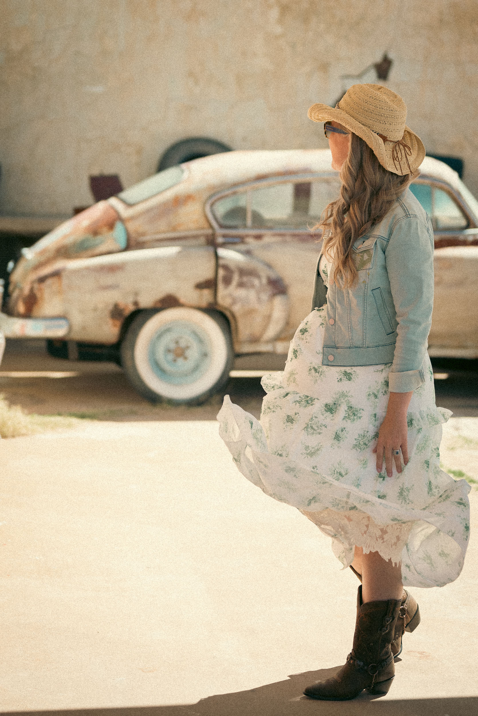 woman in a candid scene with an old classic car in the background and dress blowing in the wind.