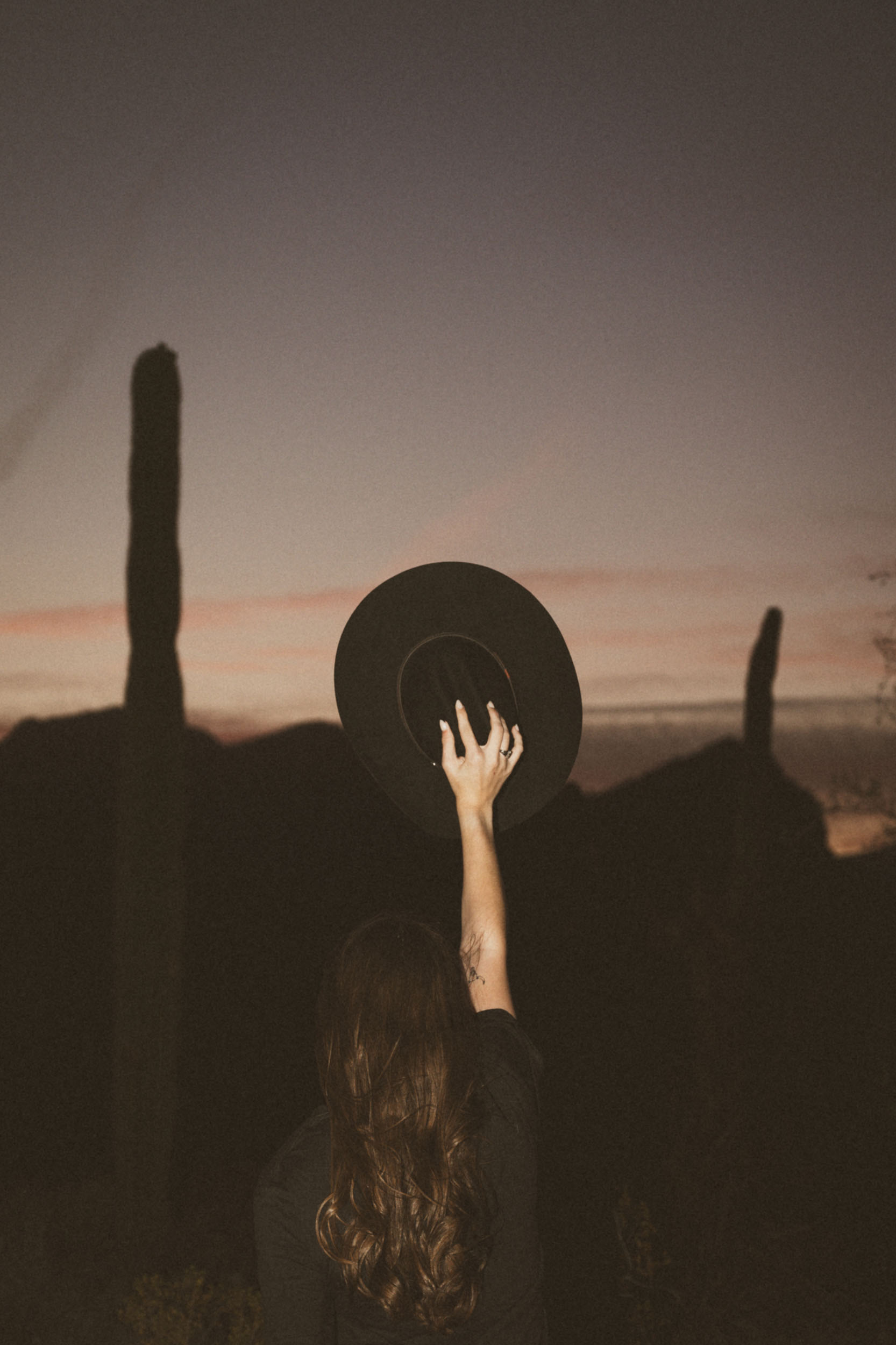 young woman, cowboy hat salute to the sky in a dark desert scene at dusk.
