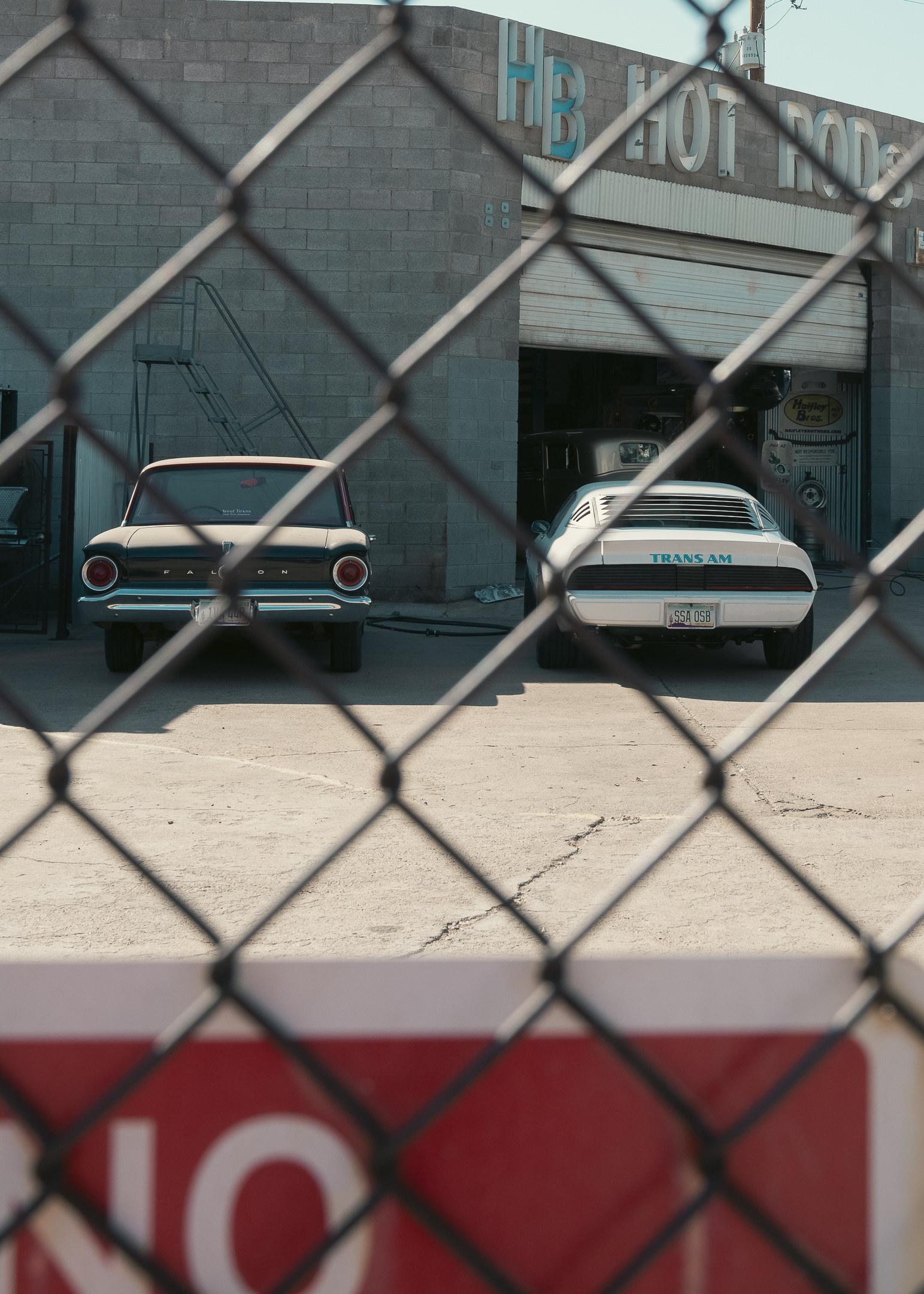 Muscle cars through chain link fence.