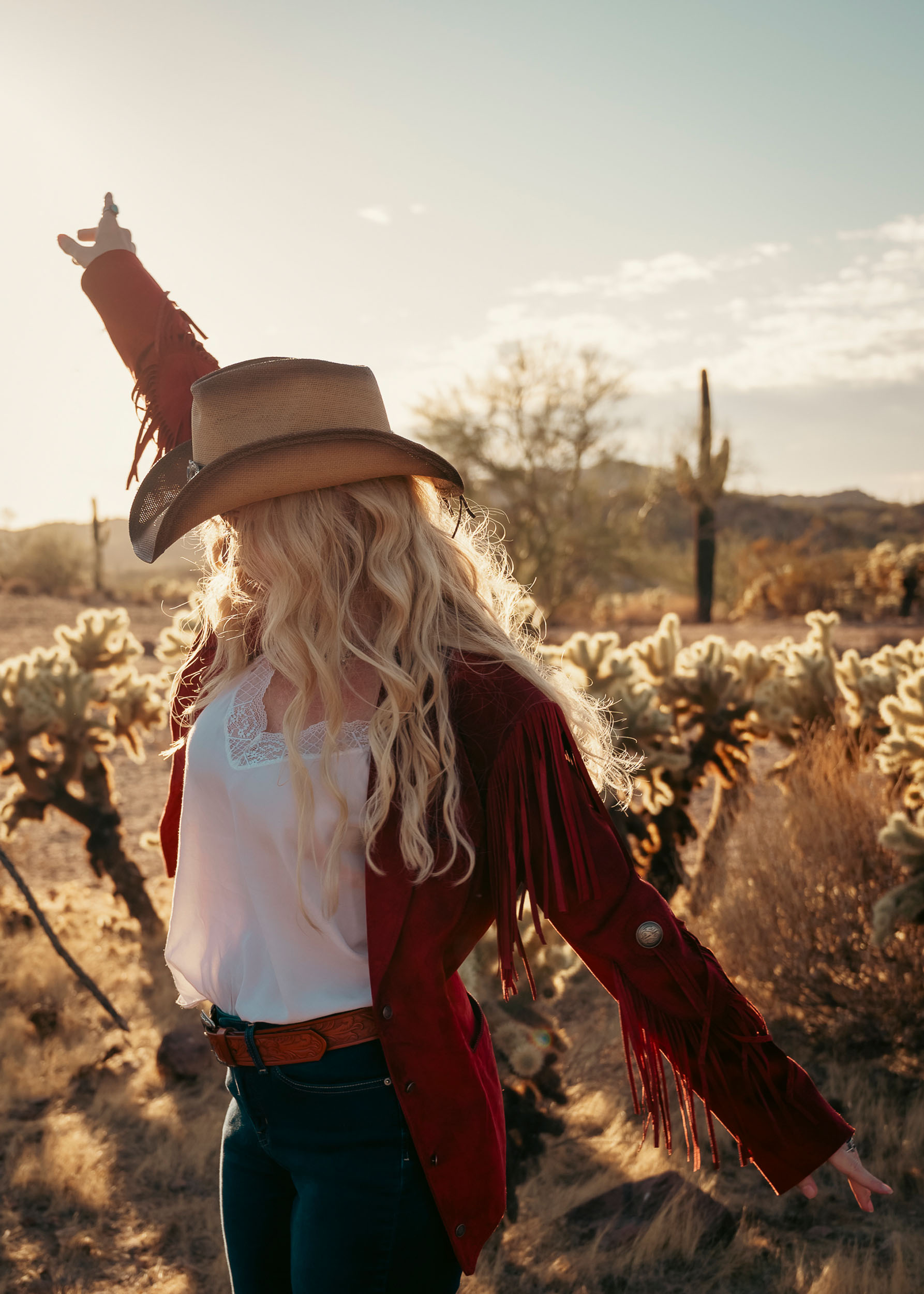 Woman in western clothing pointing to the sky in the Arizona desert during golden hour